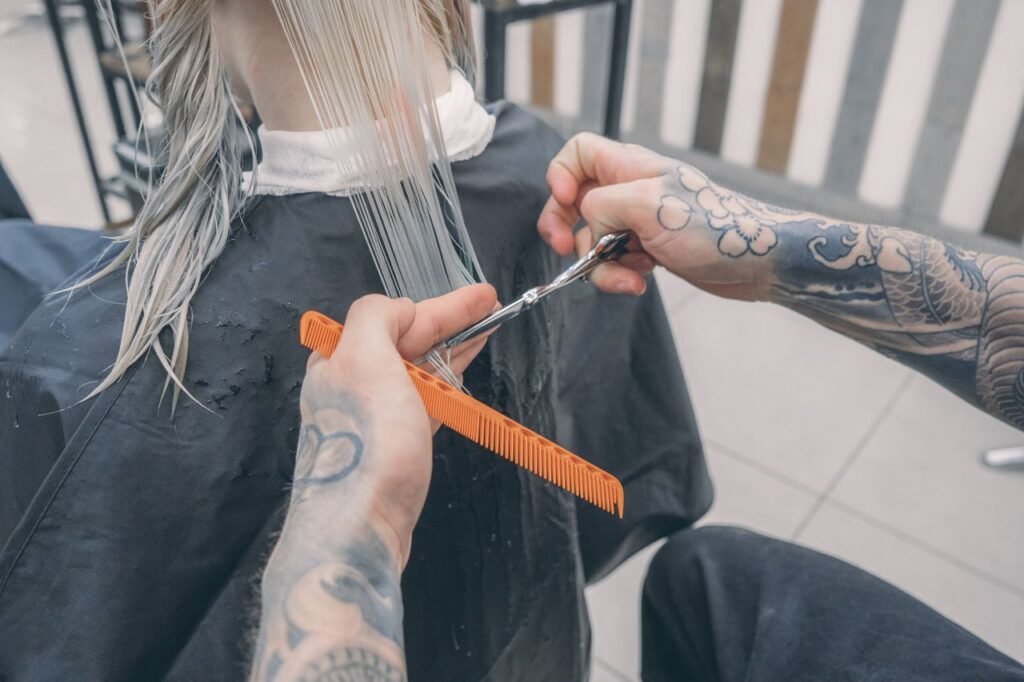 Close-up of a stylist's tattooed hands cutting wet hair in a modern beauty salon.